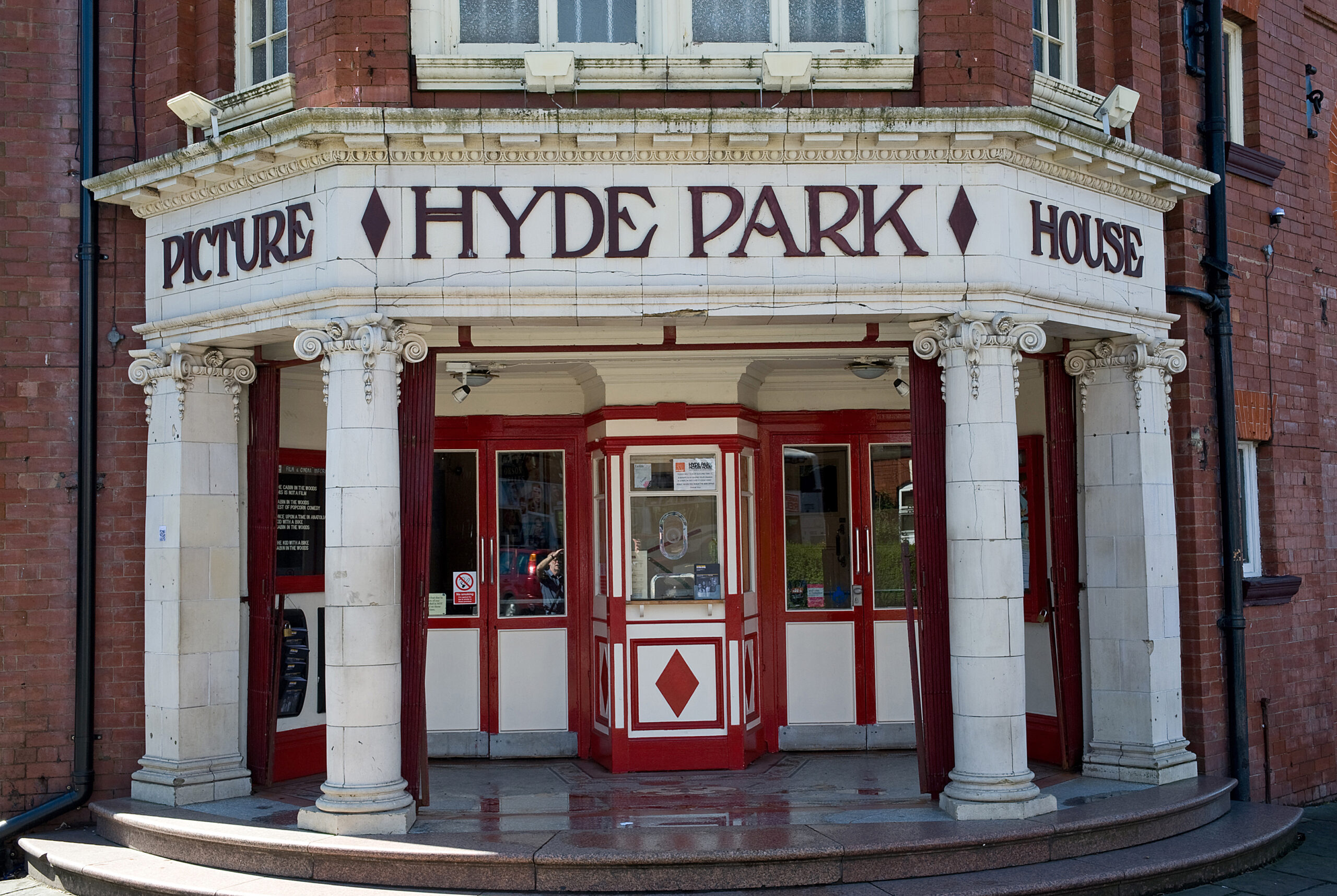 the front door of hyde park picture house in red and white, with a ticket booth window in the middle