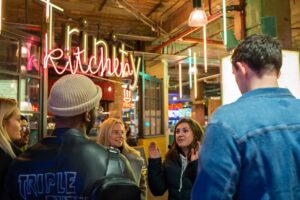 a guide hosting a group of people for a tour with the trinity kitchen behind them