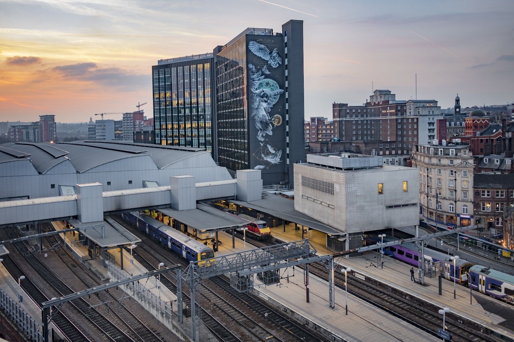 A view from above, across Leeds Train Station towards the Platform A Building which shows the large mural Athena Rising on the side of it - depicting an owl in flight.