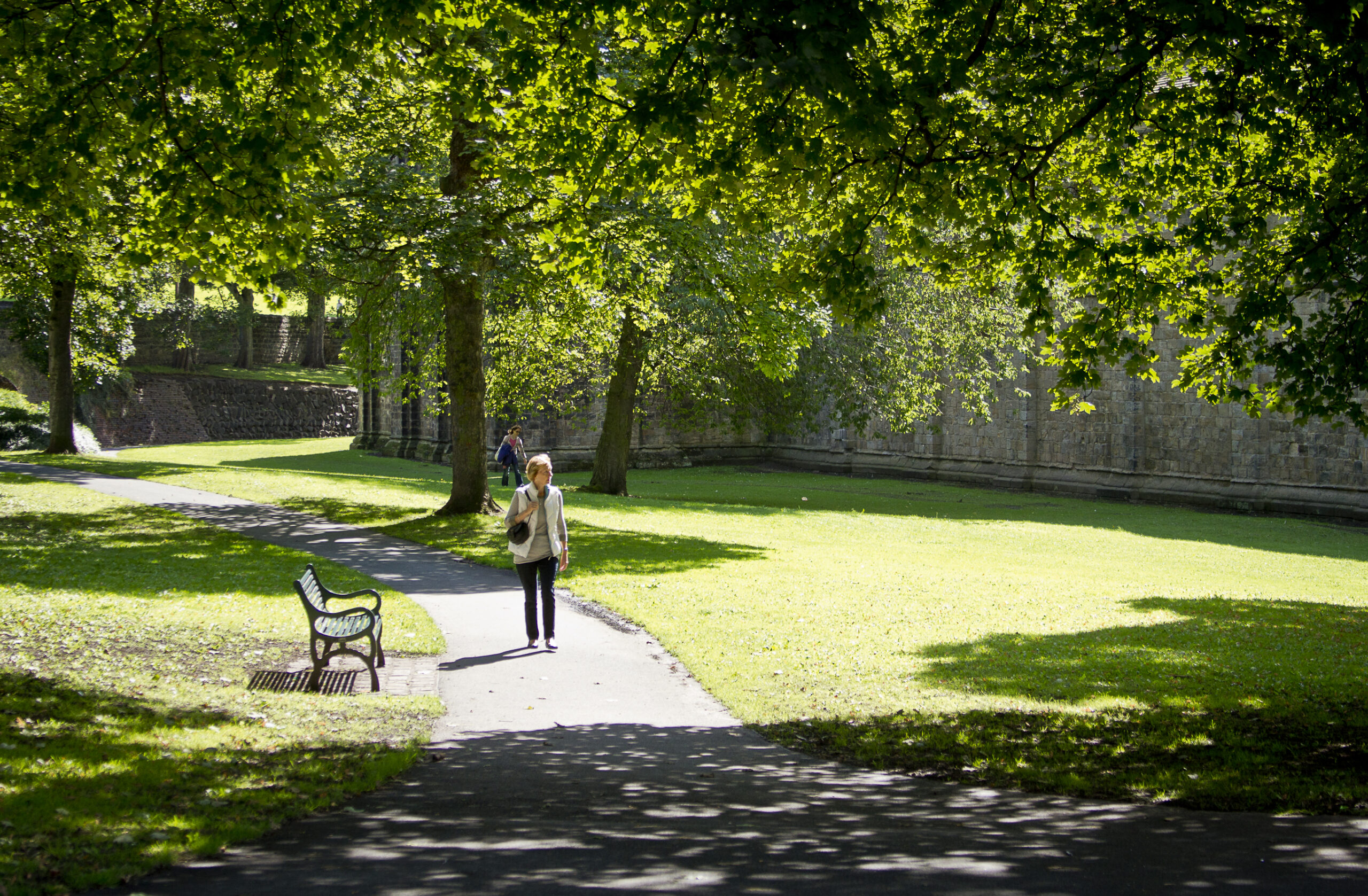 A woman walking through the gardens of Kirkstall Abbey on a sunny day - credit Leeds Museums and Galleries