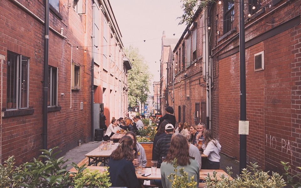 People socialising outside of Whitelocks pub in Leeds beneath festoon lighting.