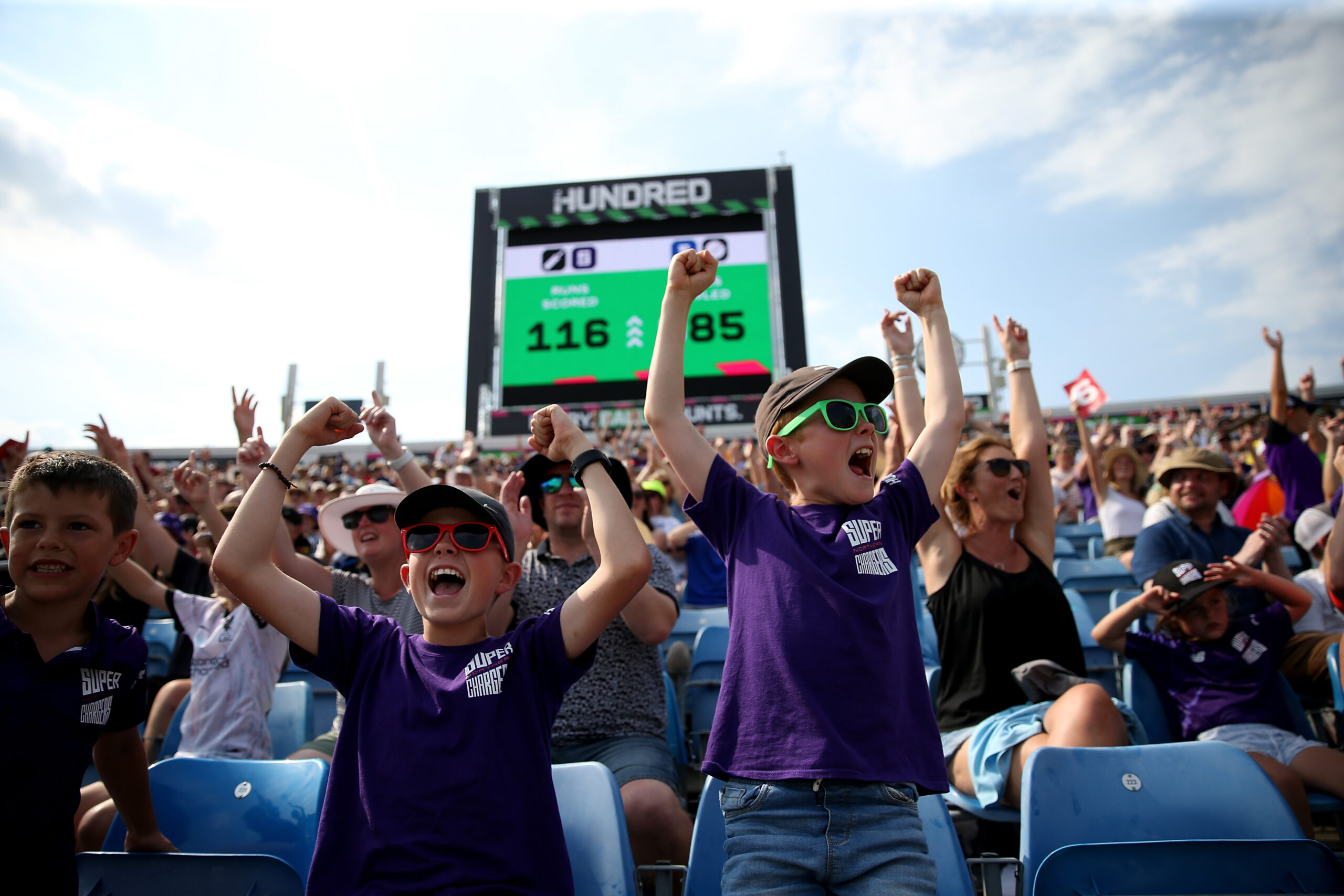 Two young boys jump up and cheer in crowds at Cricket Match