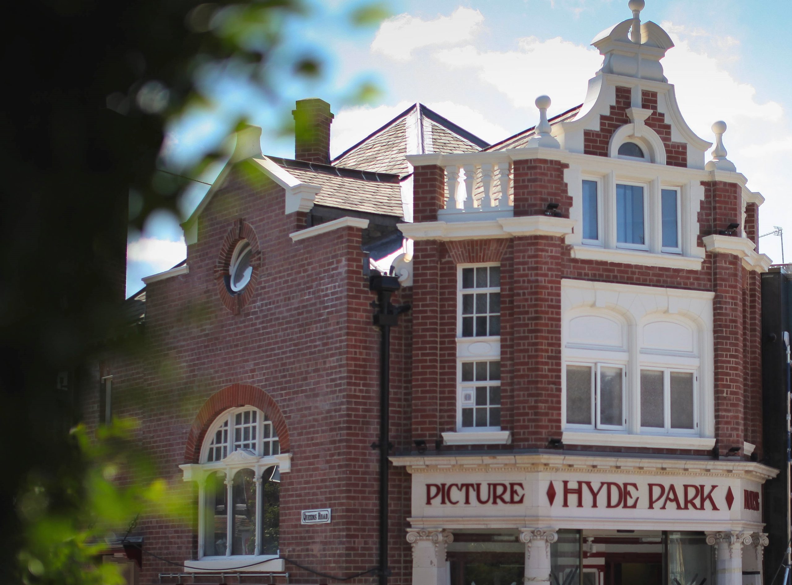 a view of a red brick building with white windows and a front door with white columns and in big red letters above hyde park picture house