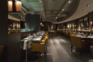 a row of tables and chairs set up for dinner with wine buckets, crockery and cutlery