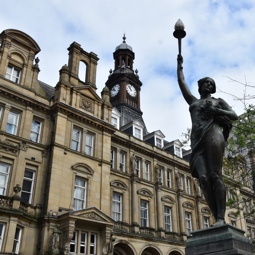 Exterior view of the Old Post Office building on City Square in Leeds, it is an ornate facade with a clock tower, in the forefront there is an iron statue raising a lantern.