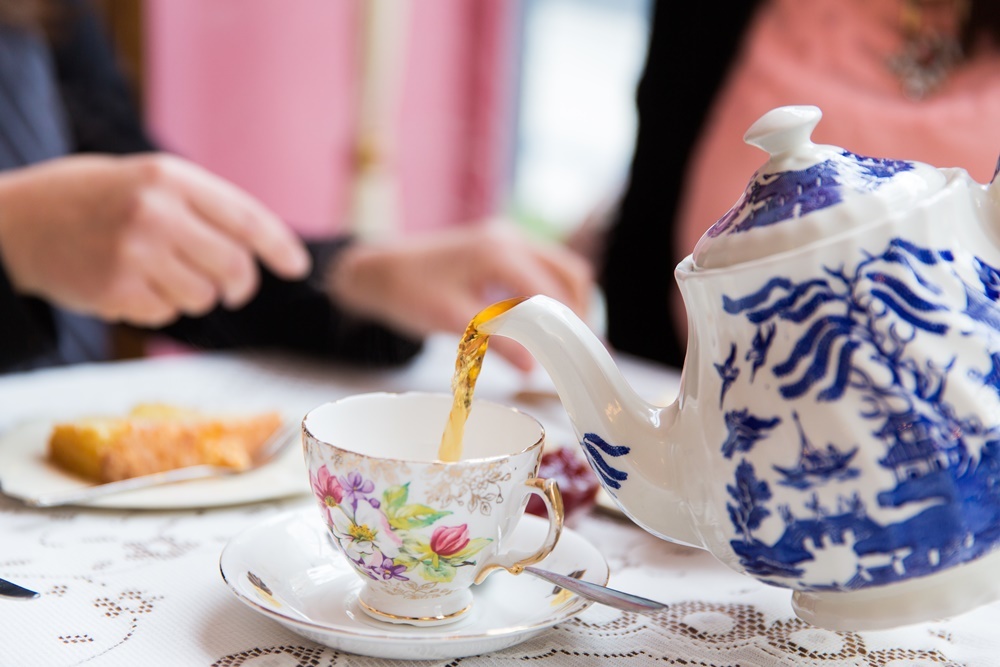 Close up of tea pot pouring tea into a china cup on a dolly adorned table. At Just Grand Vintage Tea Room