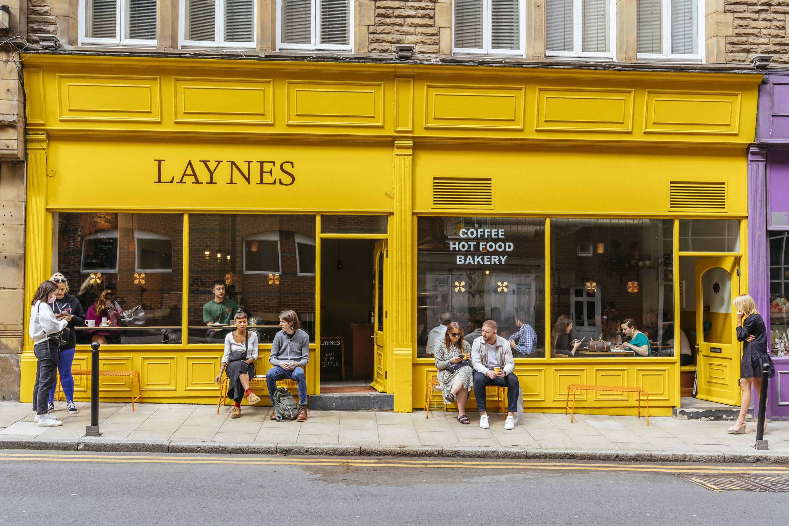 the front of laynes cafe, with bright yellow exterior, and people sitting on benches outside the windows