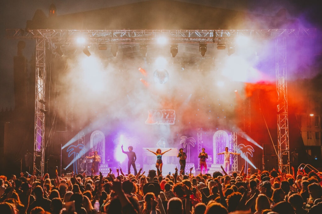 a concert scene with large crowd and group on stage with stage lights
