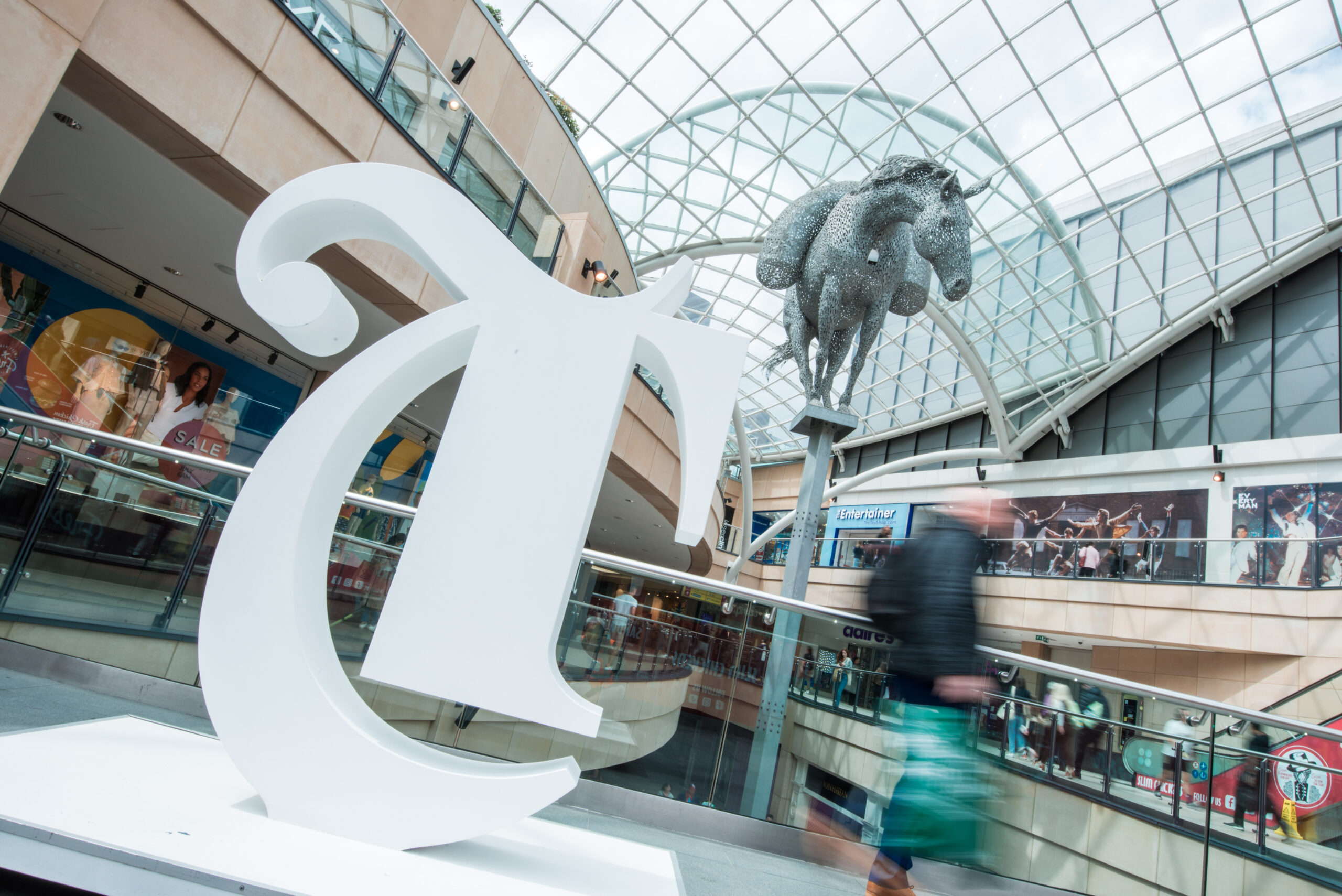 people walking around a shopping centre with a large T logo and horse statue