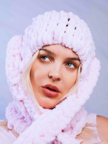 Close up headshot of performer Anne-Marie in a white wooll en hat and icy blue background.