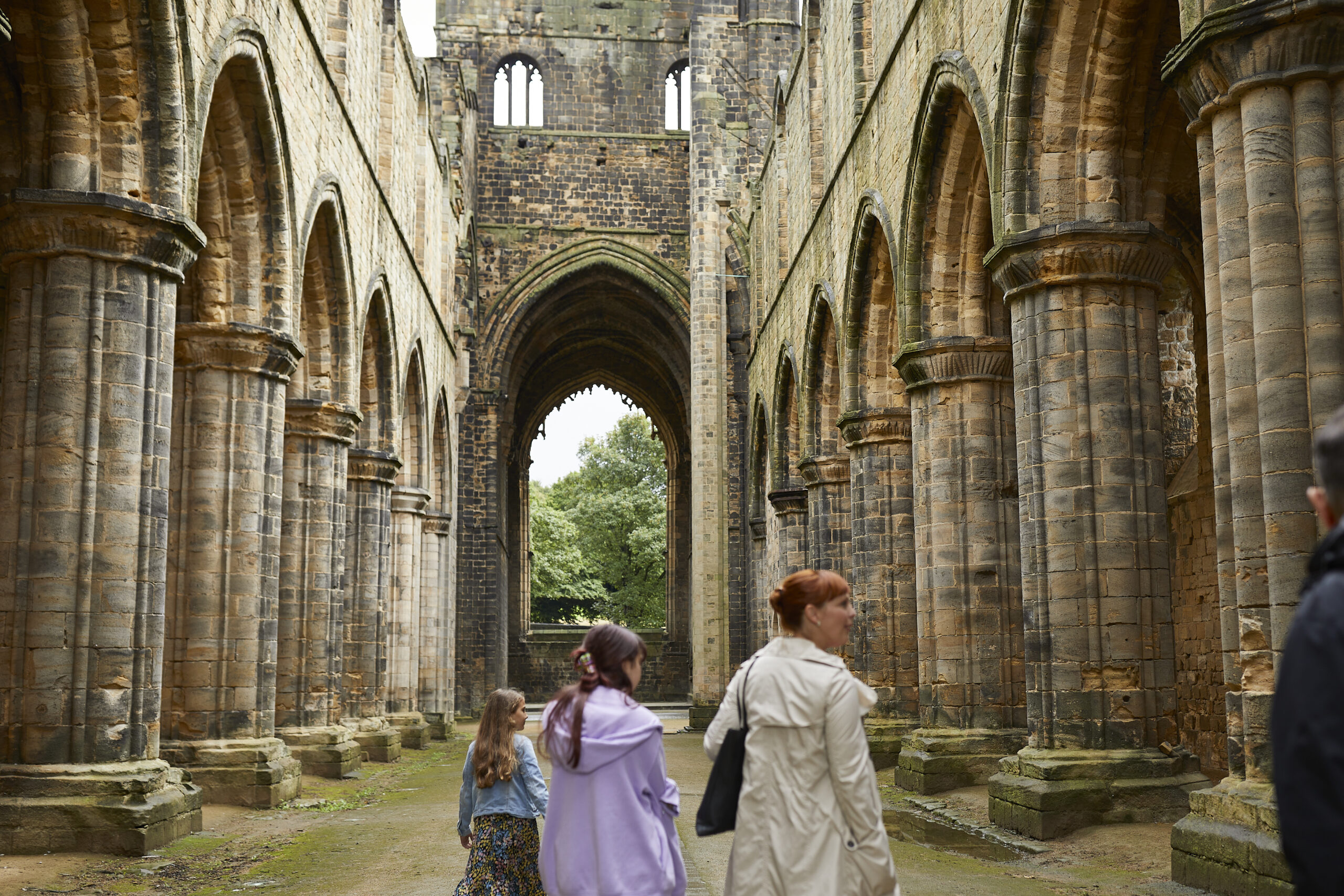 a family wandering around the ruins of an old abbey with columns and a large window space