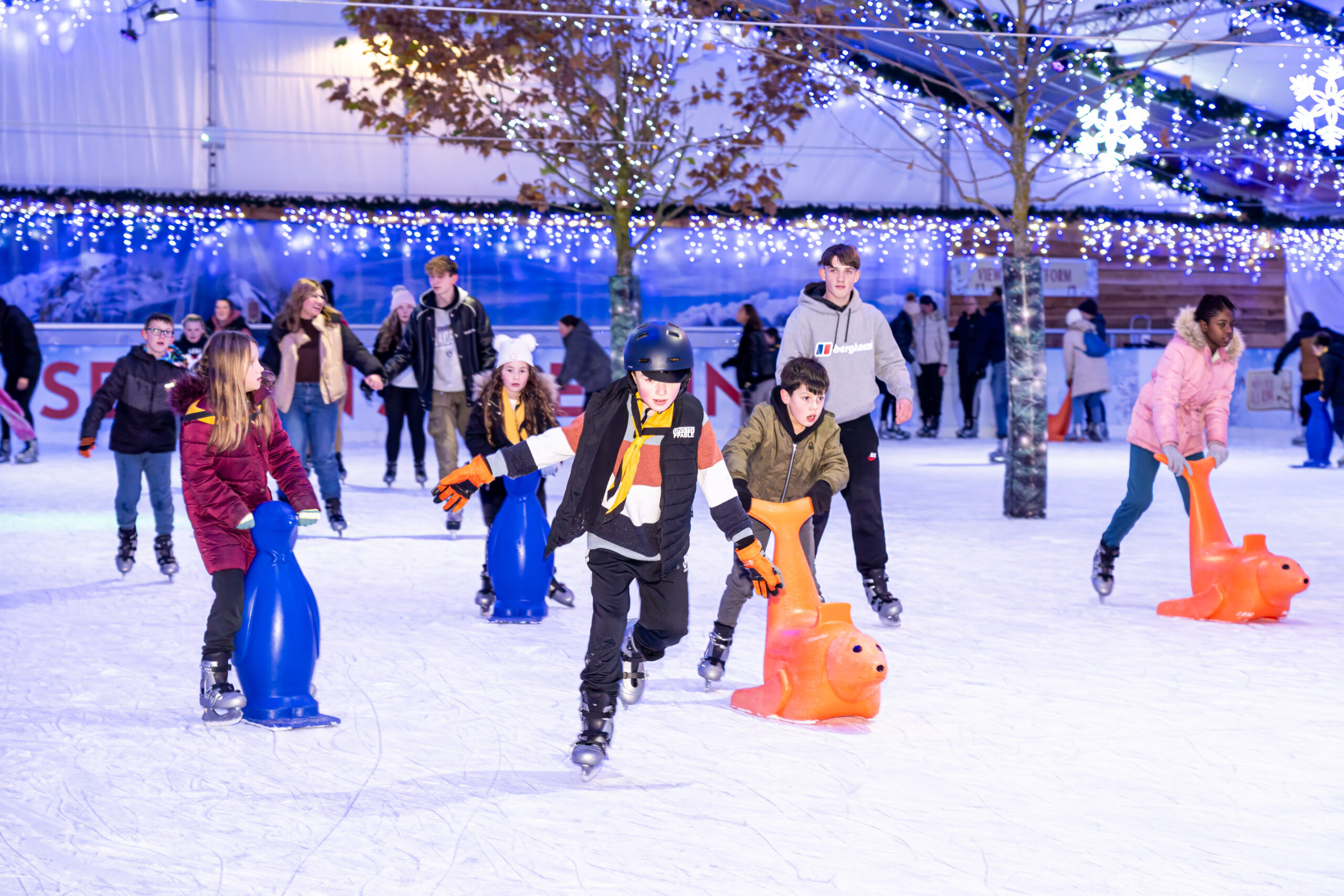 a large crowd of people ice skating including children with skating helpers