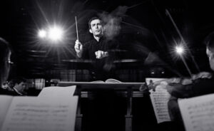 a man stood at a podium in front of an orchestra conducting