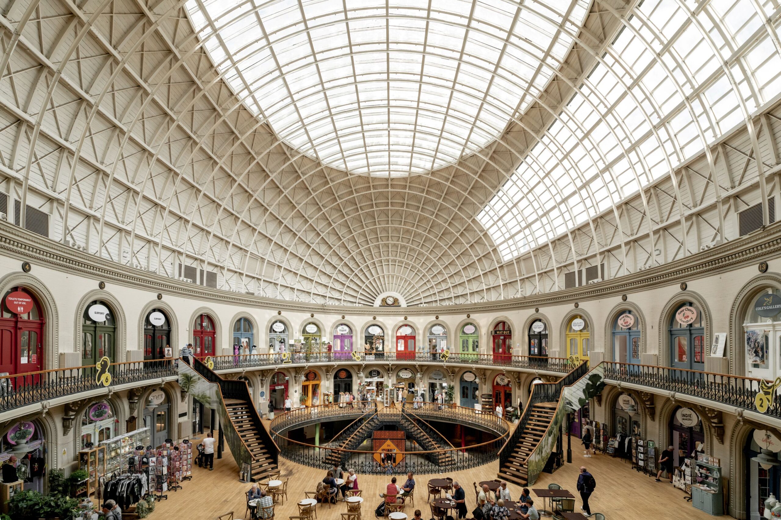 An interior view of the iconic Leeds Corn Exchange - a domed roof, colourful shop front entrances and staircases.