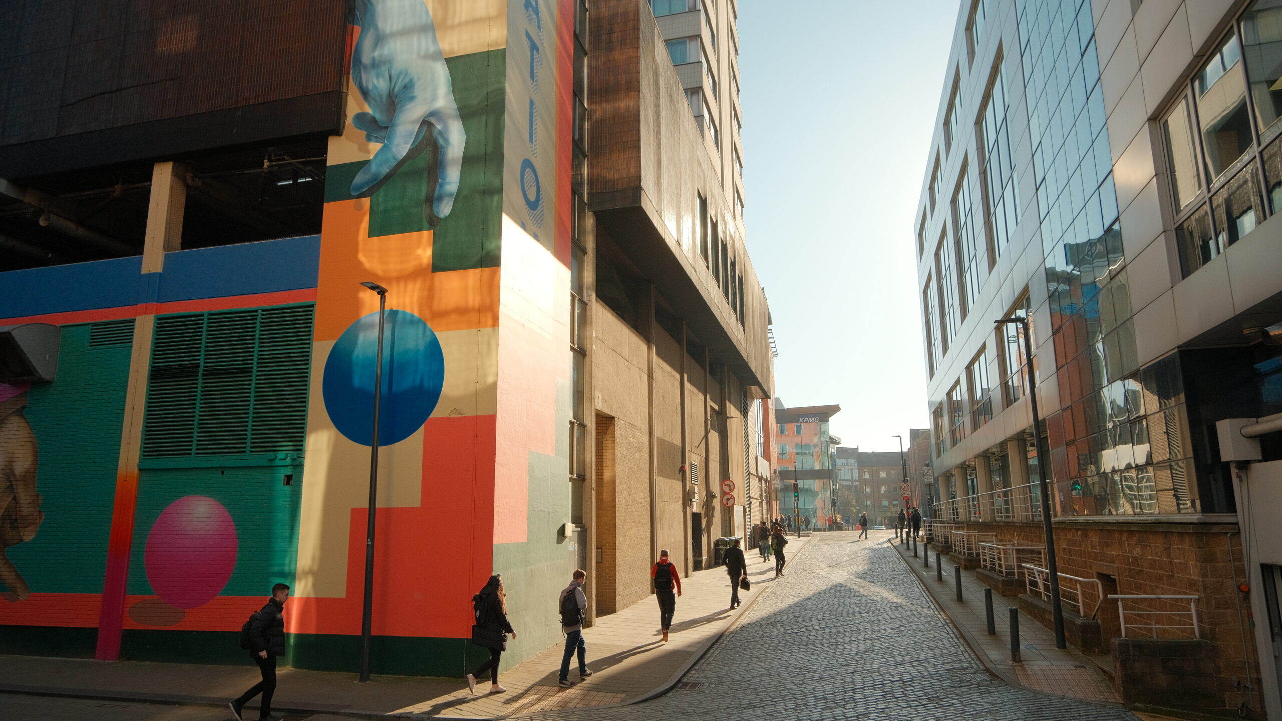 colourful street art on the side of a building with people walking past
