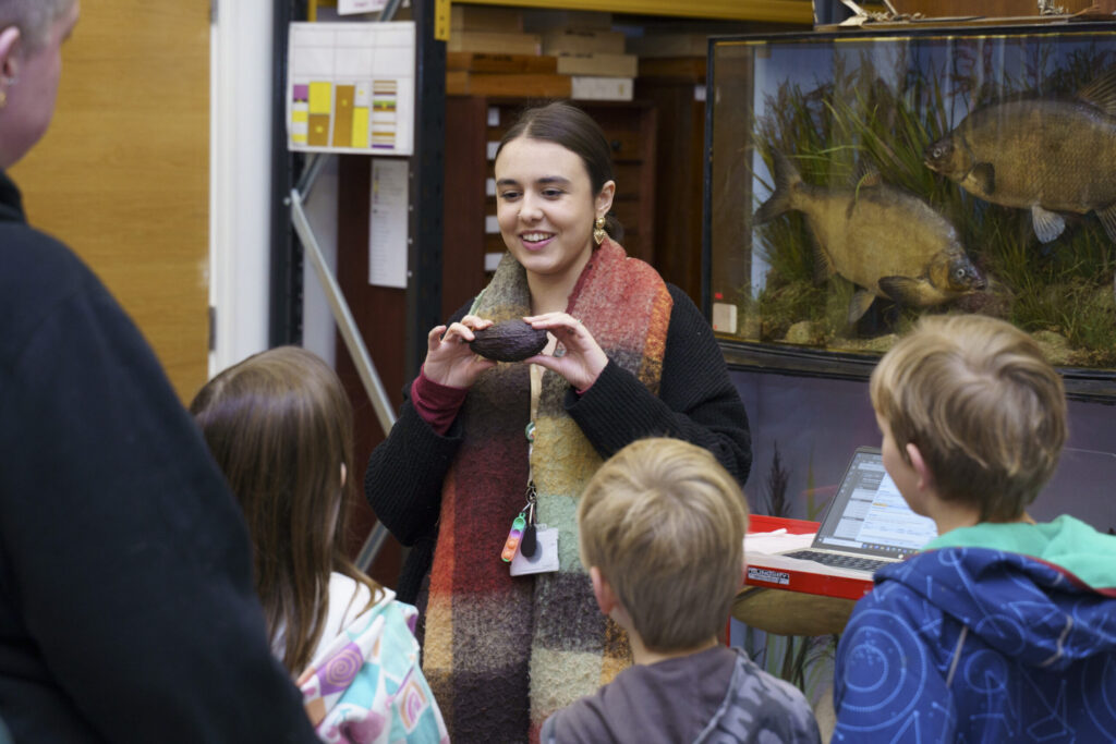 a person holding an item to show a group of children with a variety of items in cases behind them