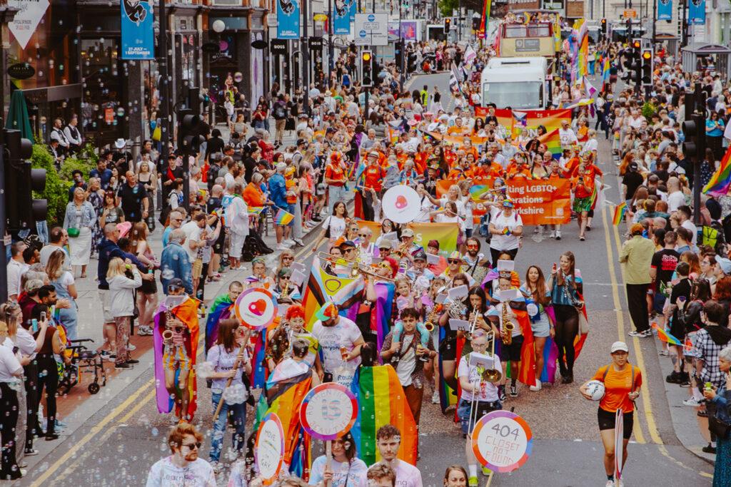 Colourful image of Leeds Pride Parade, with people marching for large crowds through a city road