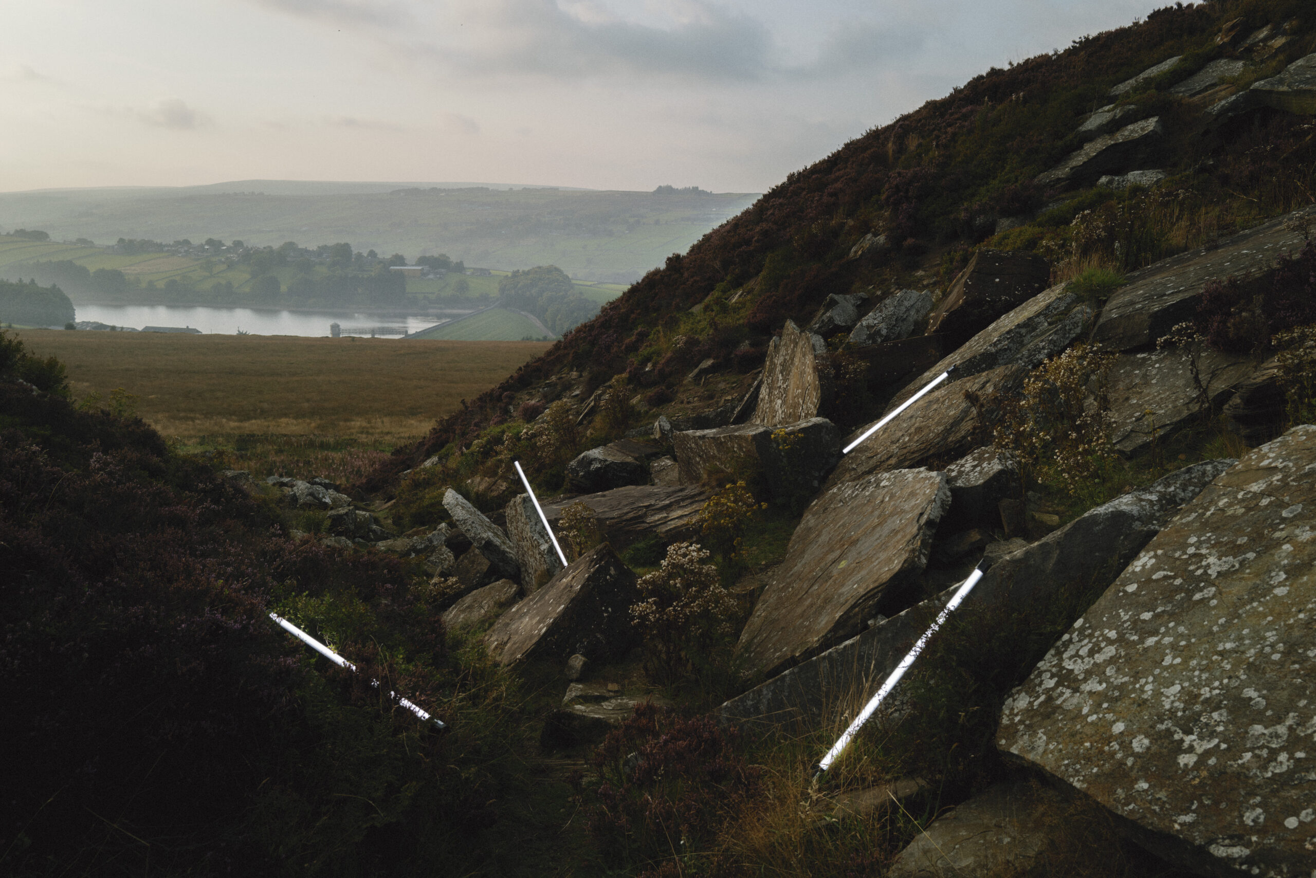 Photograph showing dramatic rocky landscape with view over hills through valley and low clouds.