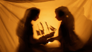two little girls playing with a ship model behind a curtain