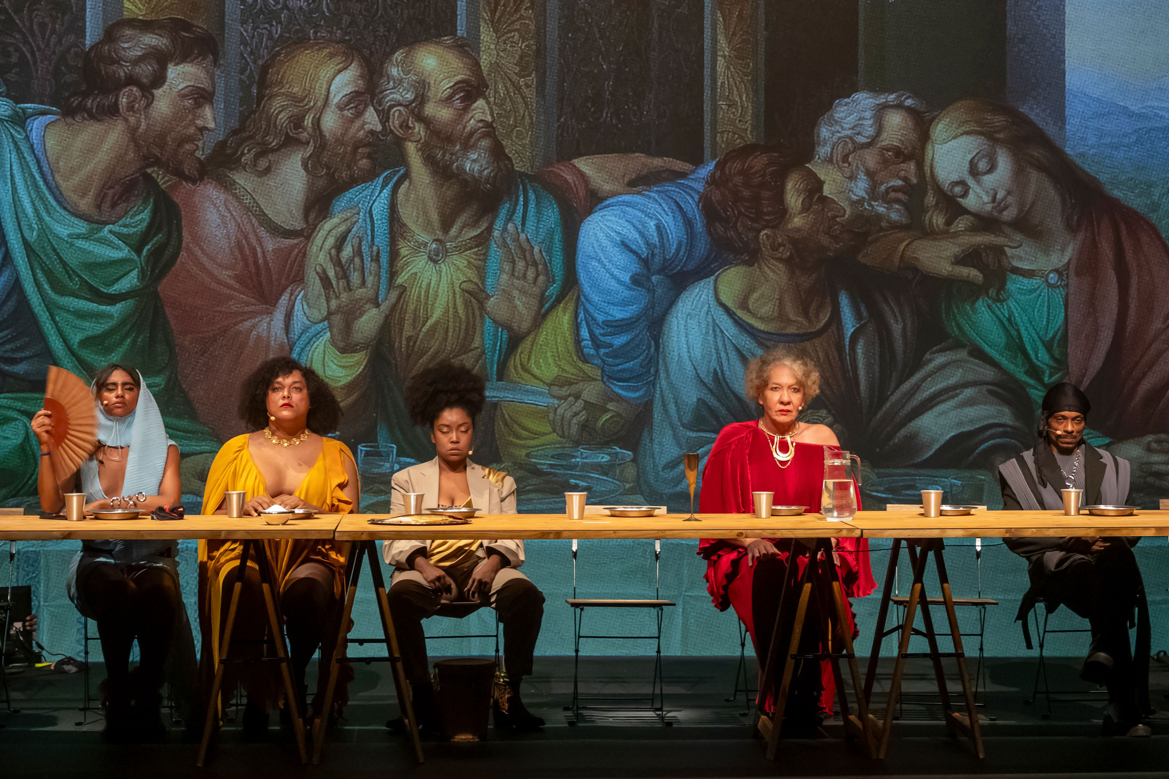 Performance of the last supper pictured with four women at a table seated and staring at the audience.