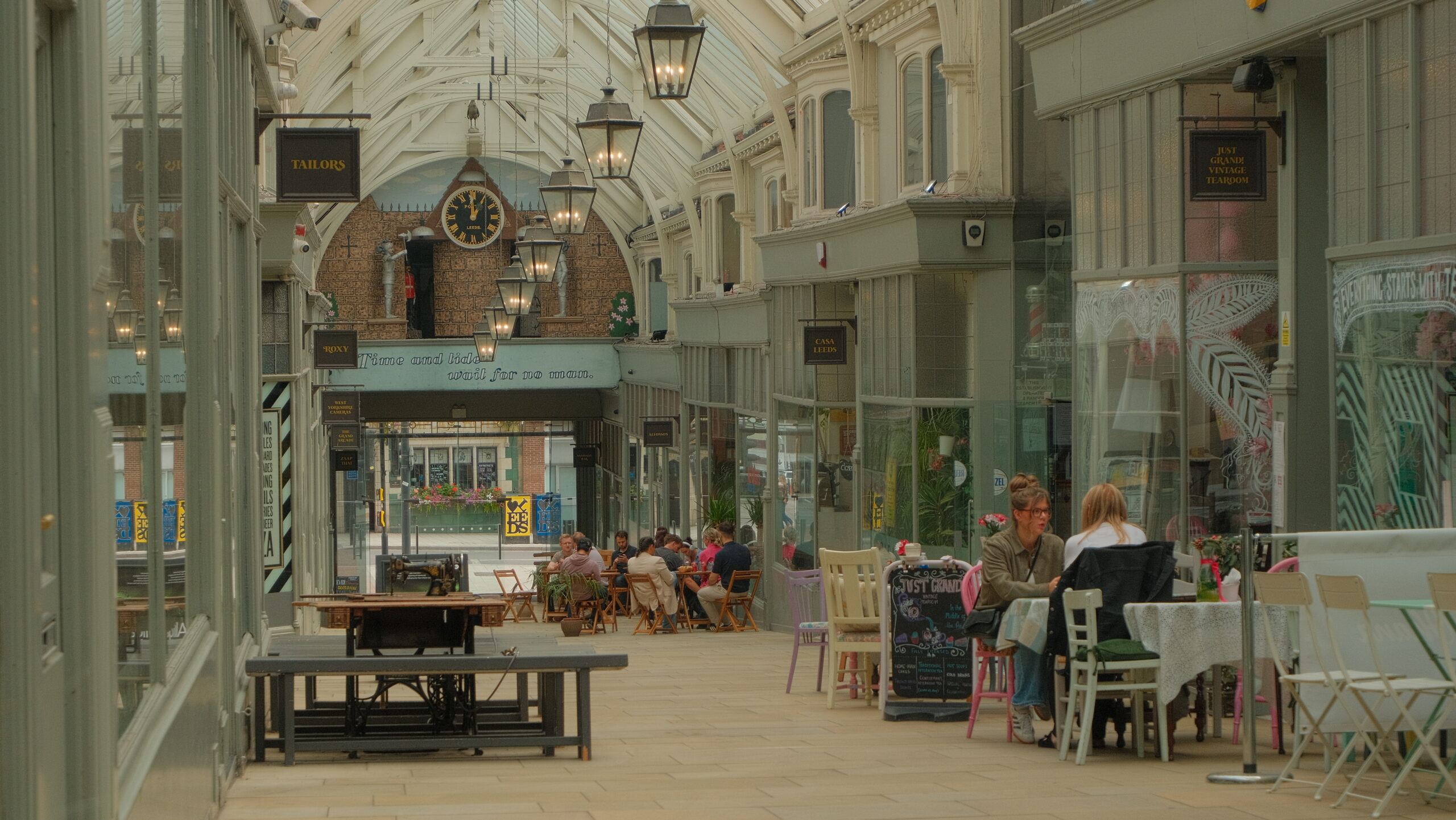 a covered arcade with tables and chairs outside shopping units on either side
