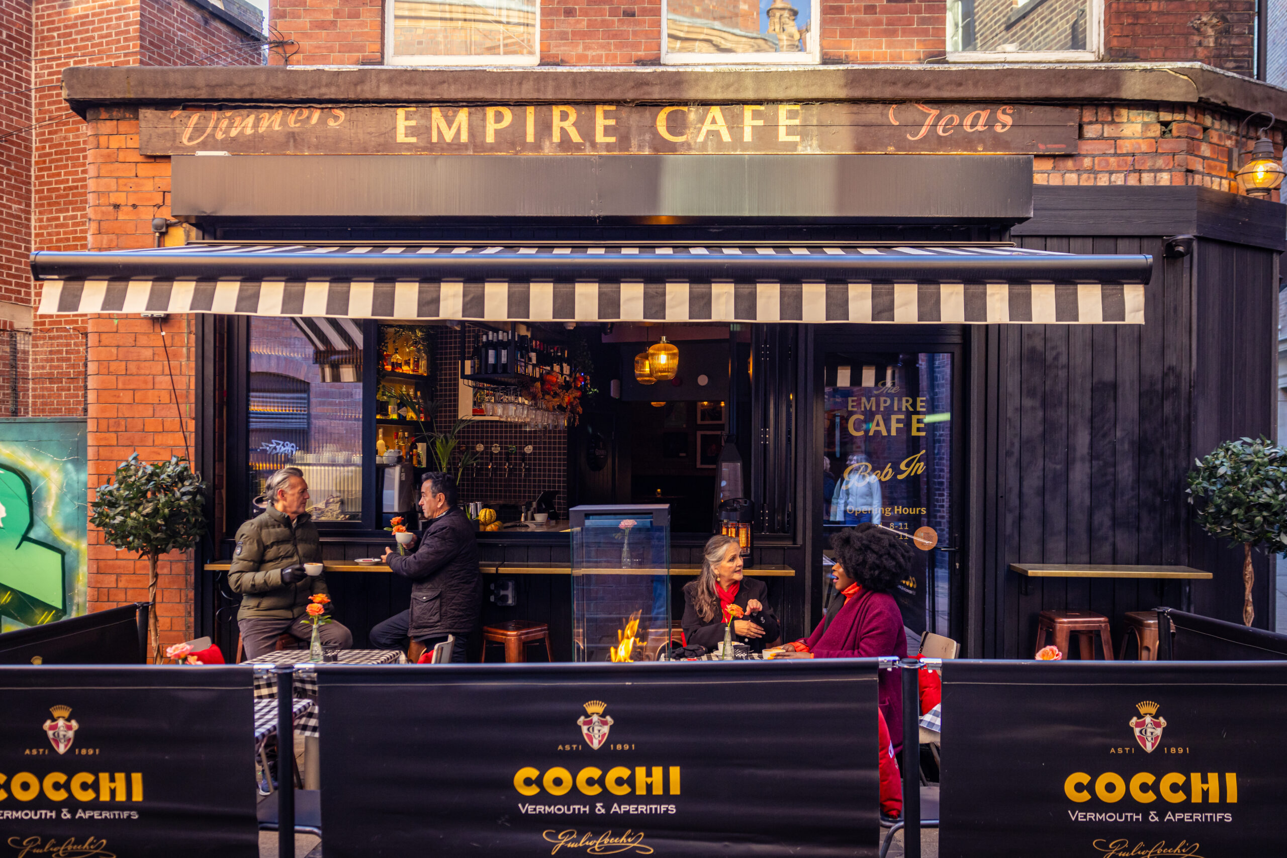 group of people sat outside a cafe with a canopy above them