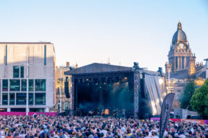 crowd of people watching musicians on a stage with the clock tower of the town hall in the background