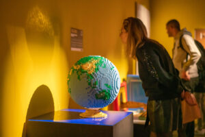 a globe made out of lego with a person looking at a description on the wall beside it