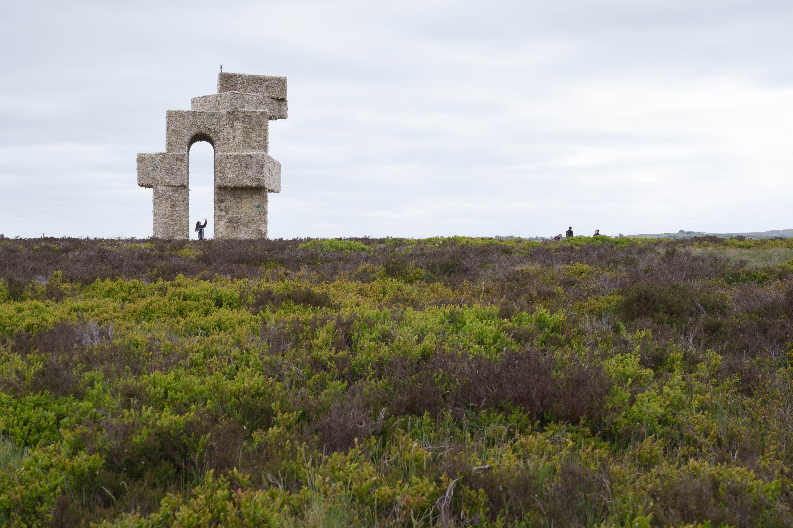 Sweeping moors landscape with a huge sculptural structure on the horizon with people approaching and beneath for scale.