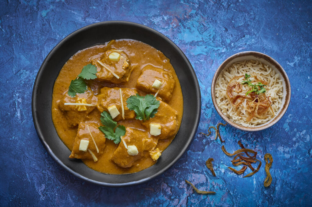a blue table with a bitter chicken curry and a bowl of rice 