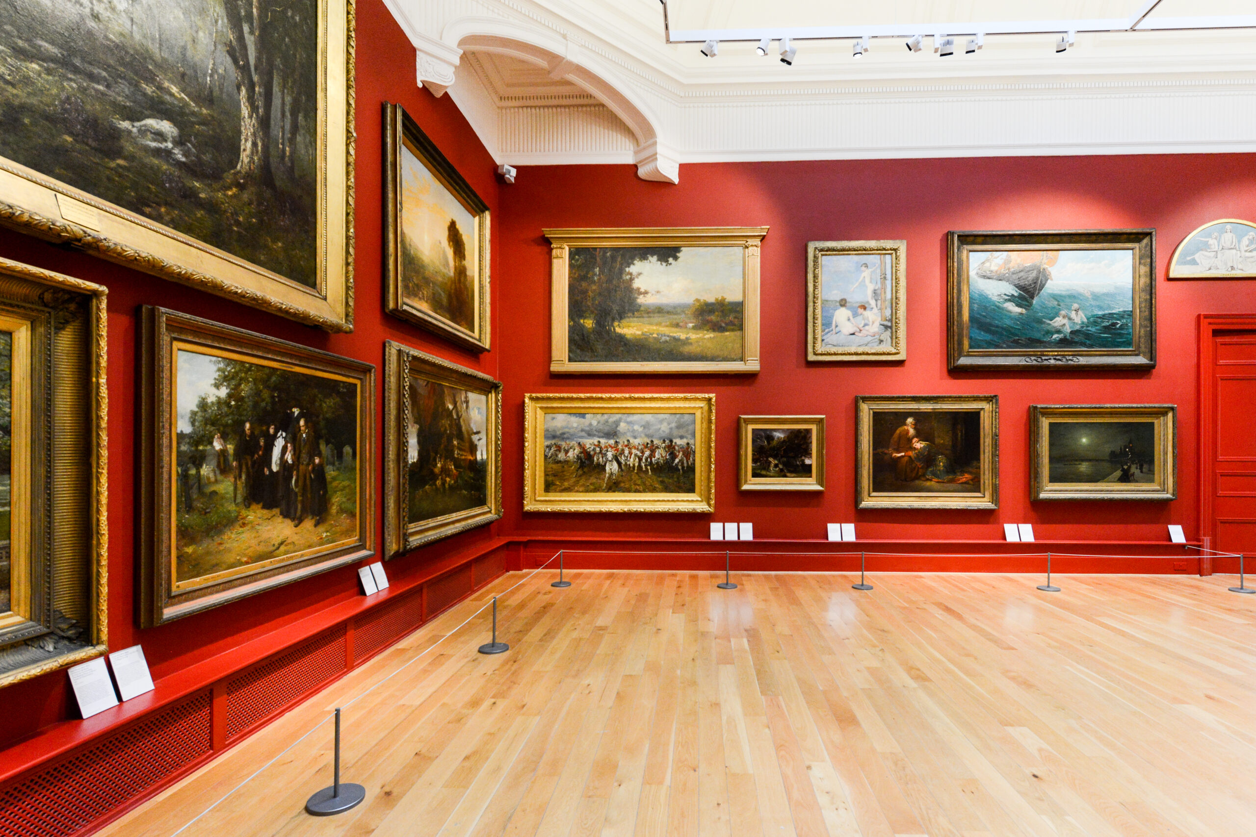 a gallery, red wall with it covered in paintings in ornate gold and wooden frames