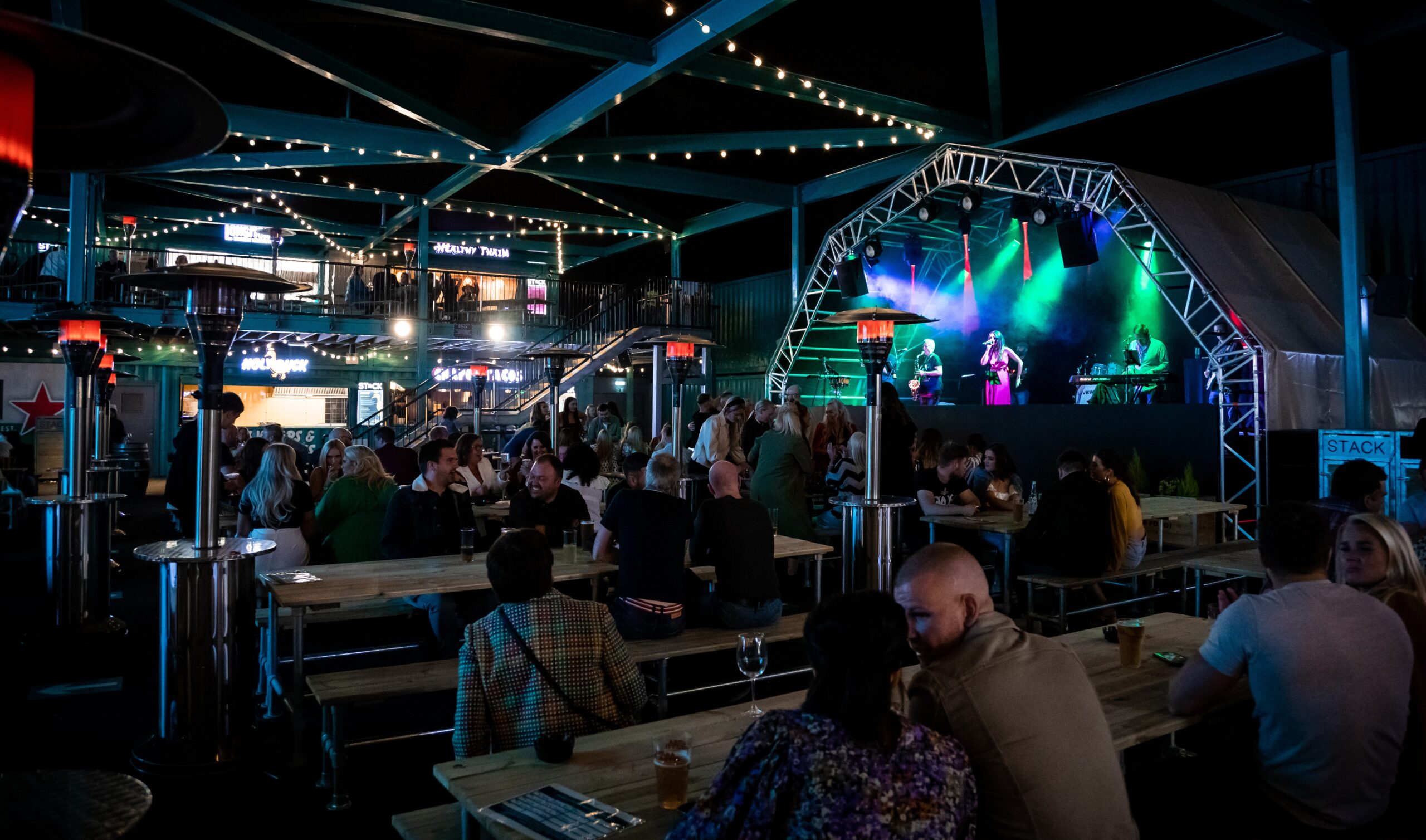people sat at picnic tables at night watching someone perform on a large stage