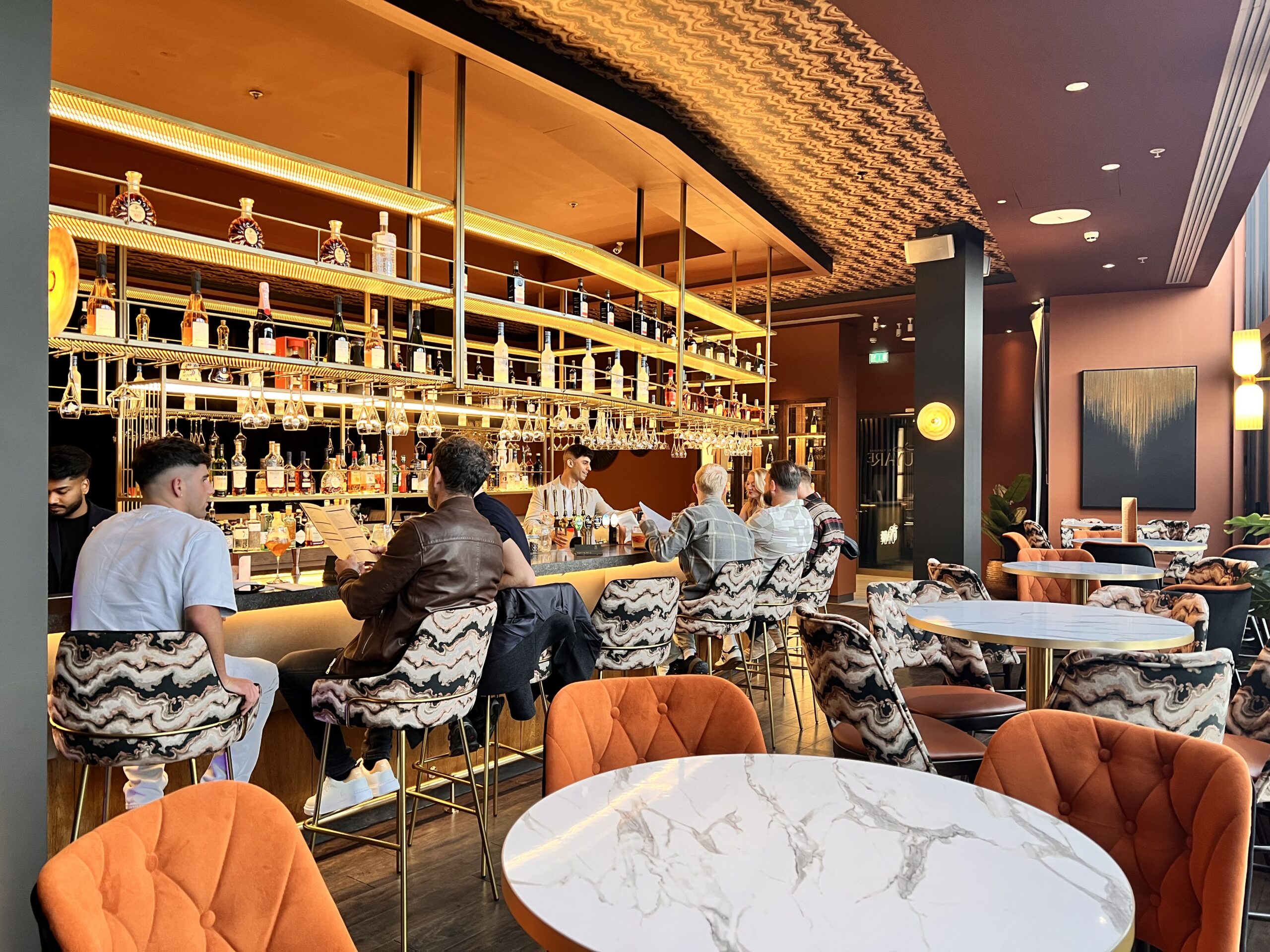 Interior view of Uyare restaurant showing the bar area with people seated and drinking, and bartenders making cocktails.