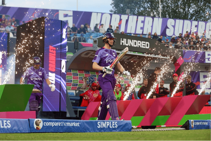 a cricket player holding their bat and wearing a helmet walking out onto the grass