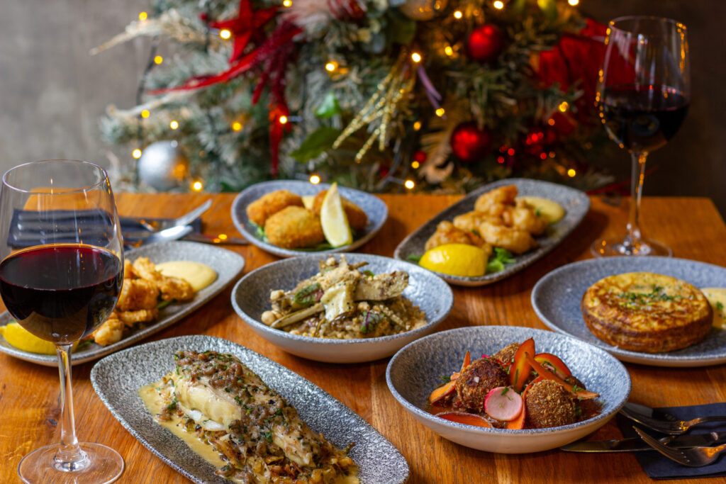 a dining table filled with plates of food and some wine glasses in front of a christmas dinner