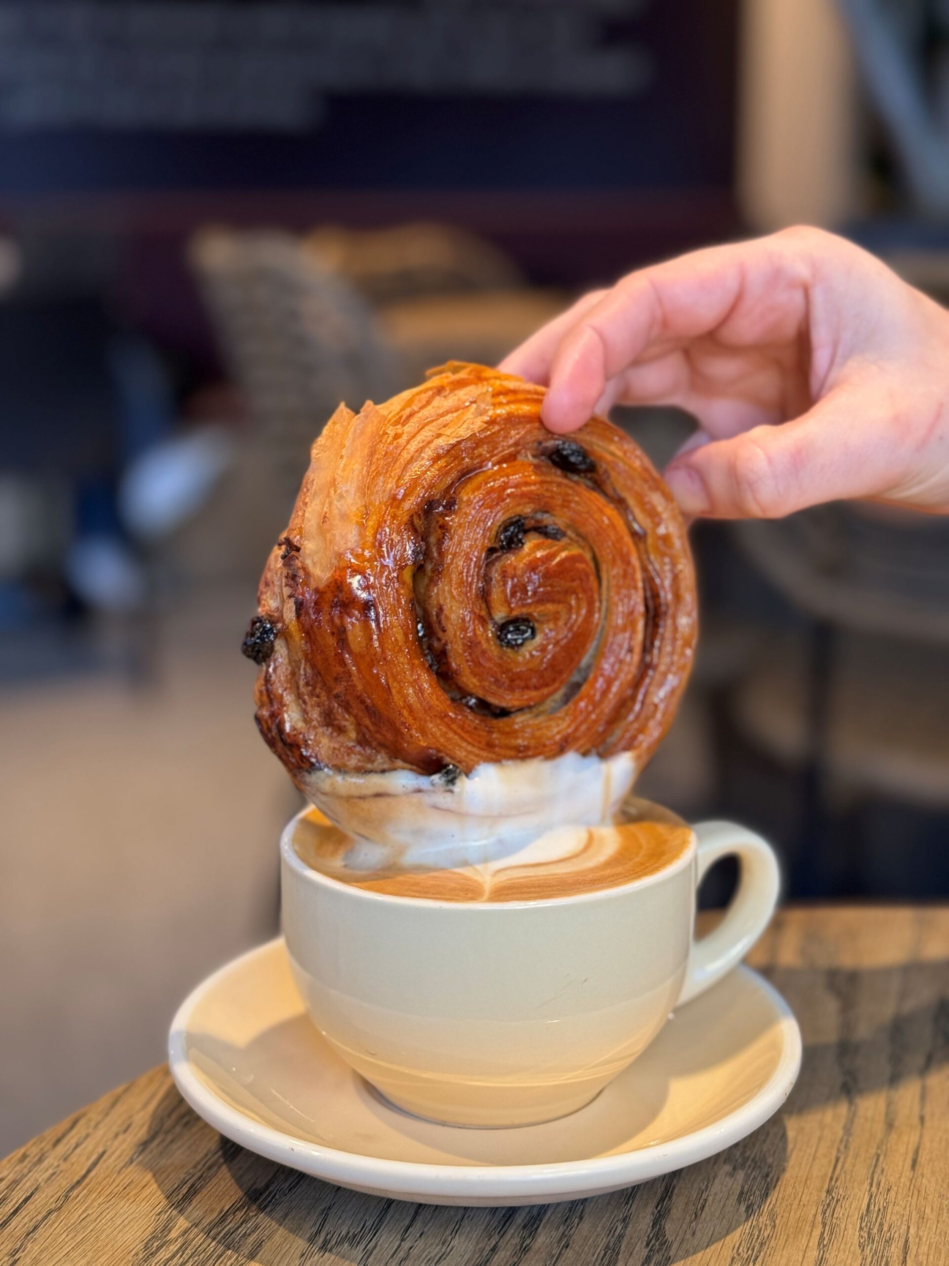 a pastry being dipped into a coffee with whipped cream on top