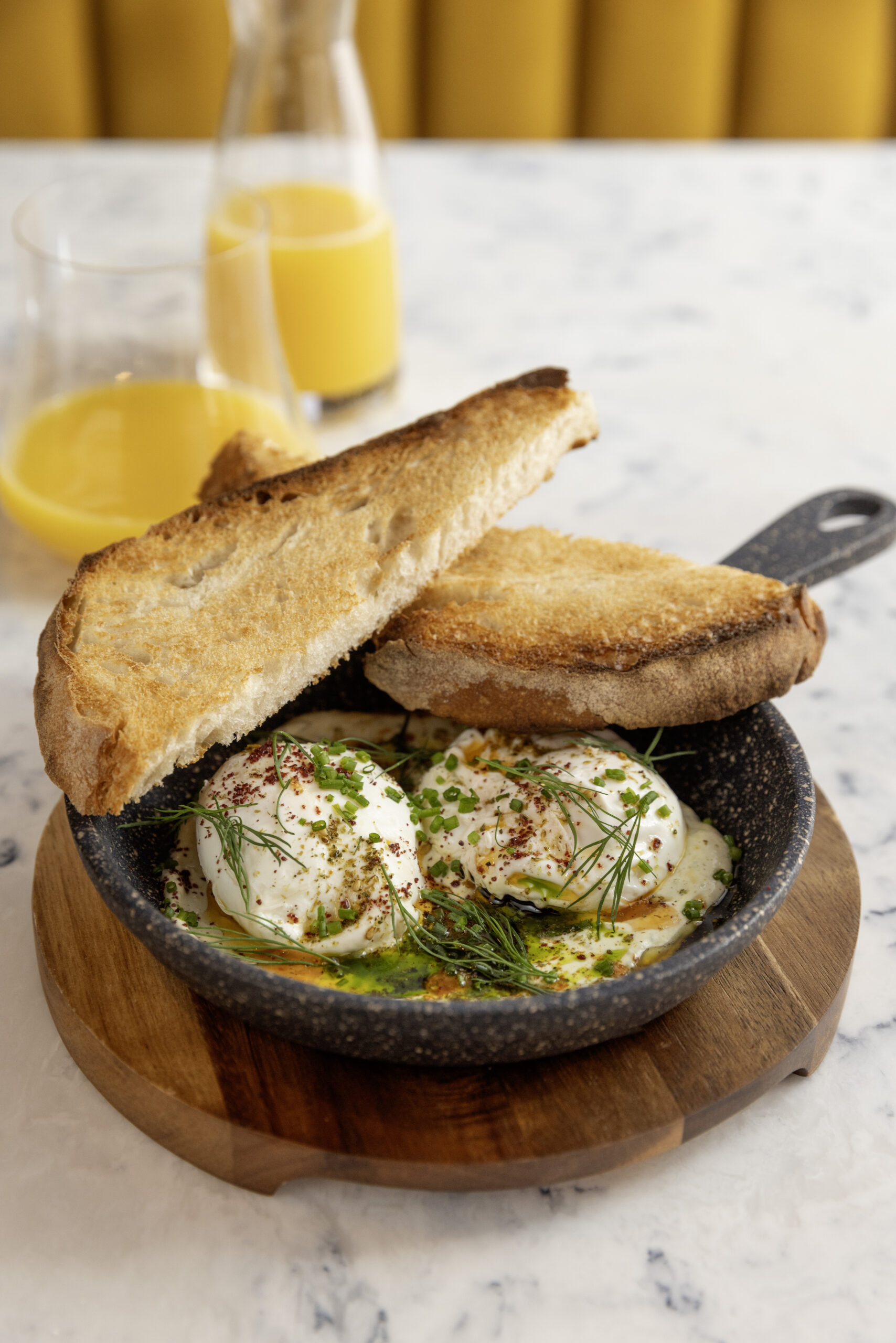 a bowl of runny eggs and toast with glasses of orange juice