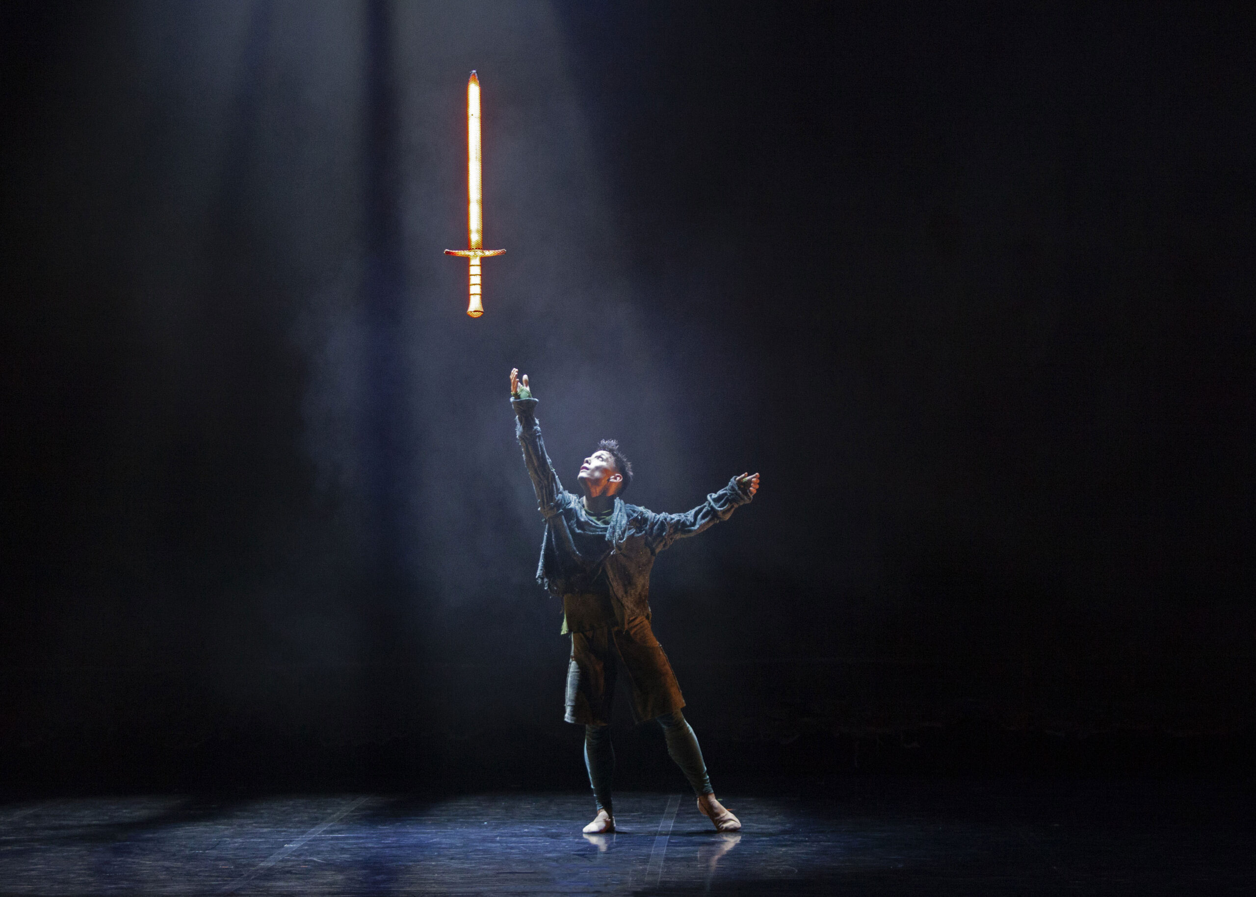 an actor on a stage reaching out for excalibur, a sword floating in the air