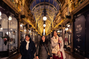 three women walking through an ornate shopping arcade with christmas lights
