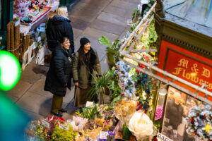 two women looking a floral stand in a market