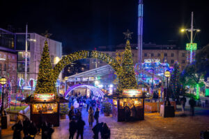 a christmas market with funfair rides and an archway with 2 christmas trees