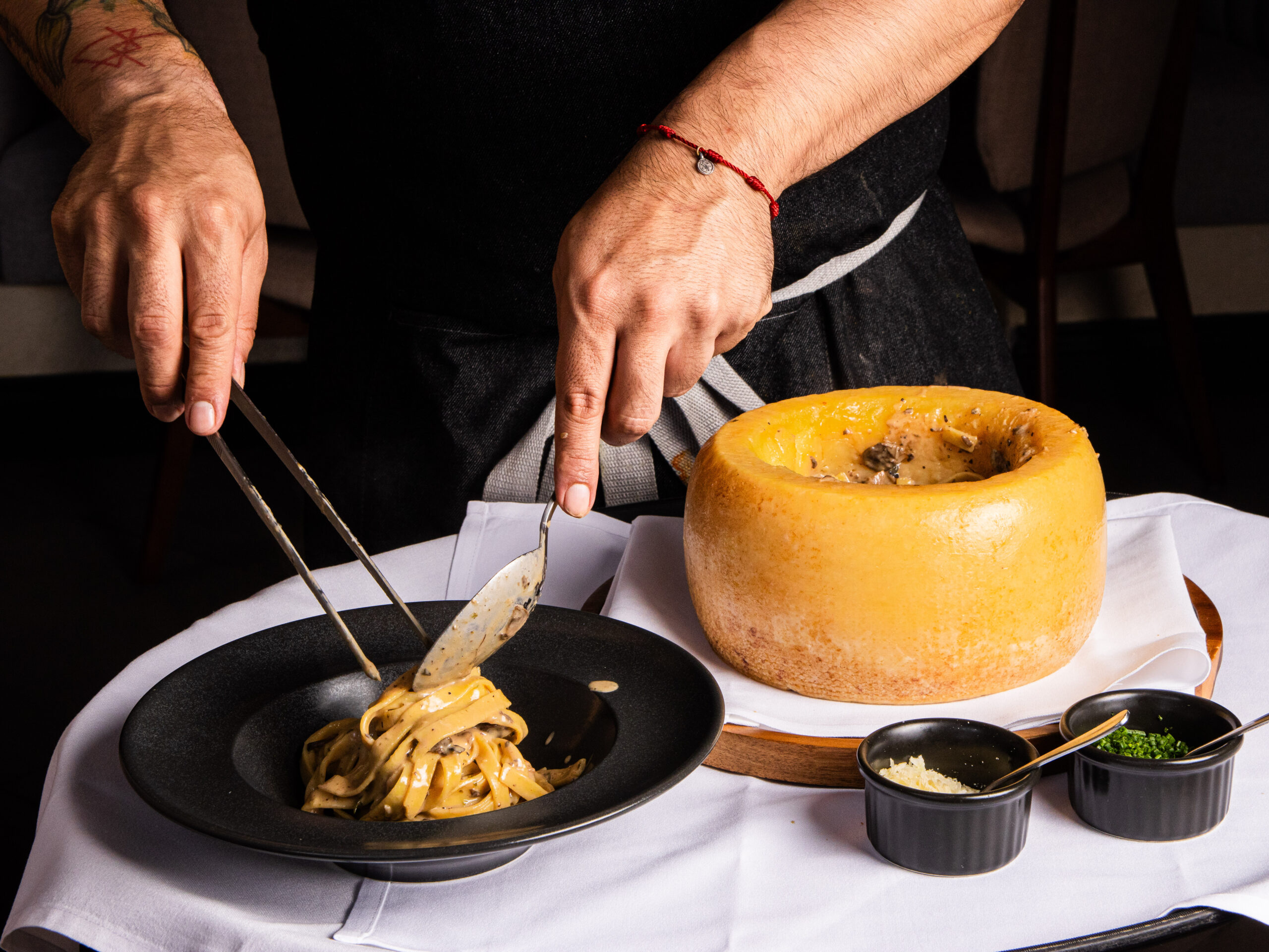 somebody preparing a pasta dish with a wheel of cheese
