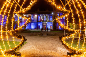 christmas tree lights in a tunnel through to a lit up historic home