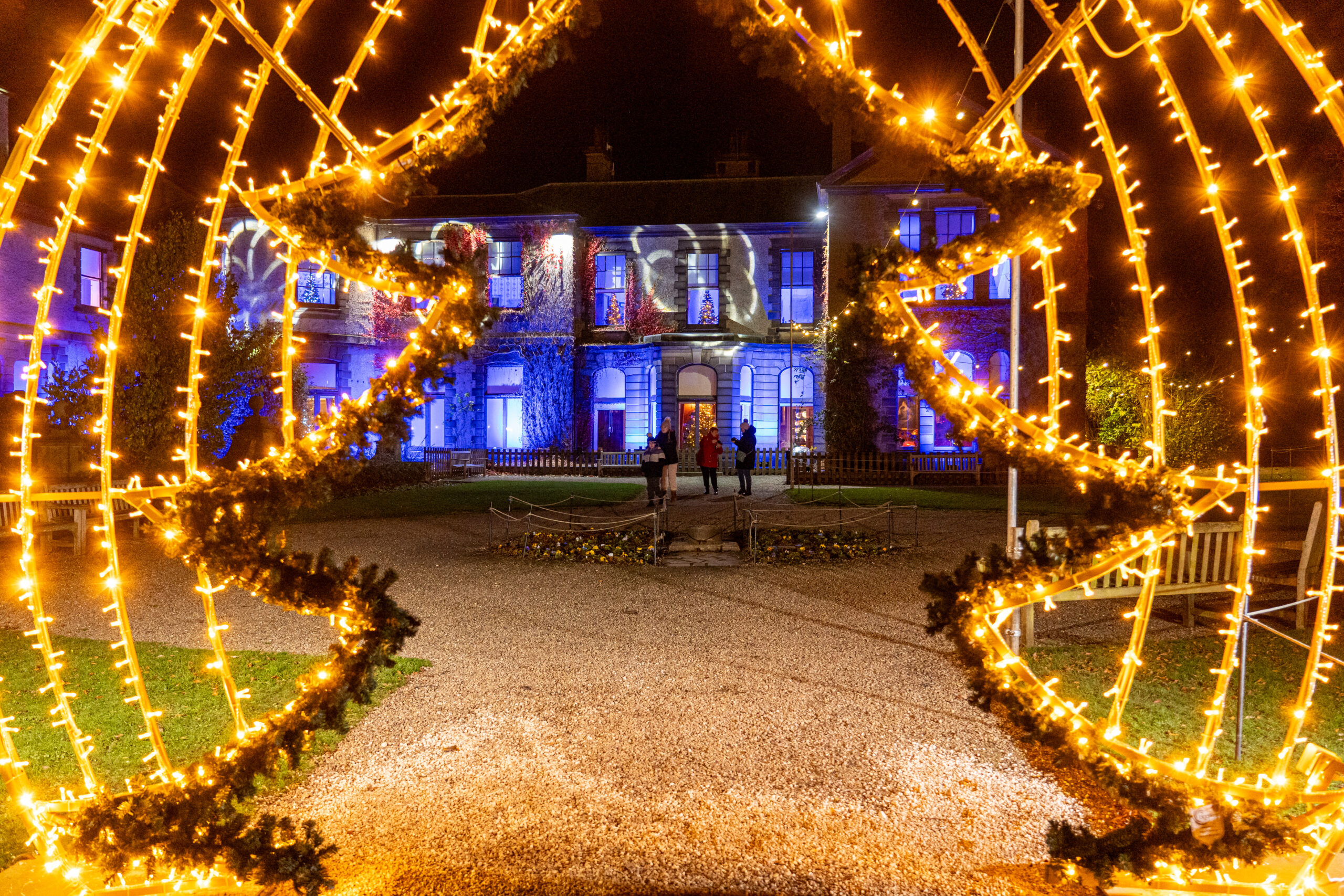 christmas tree lights in a tunnel through to a lit up historic home