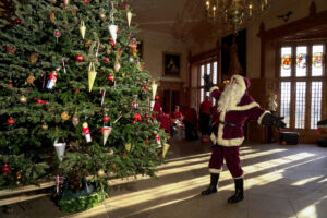 santa claus next to a large christmas tree in a historic hall