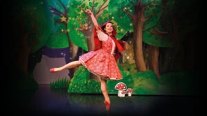 a ballet dance in a costume with a red hooded cloak infront of a forest backdrop