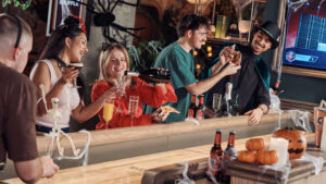 a party of people sharing cocktails, pizza and playing shuffleboard in a variety of halloween costumes and cobwebs around them