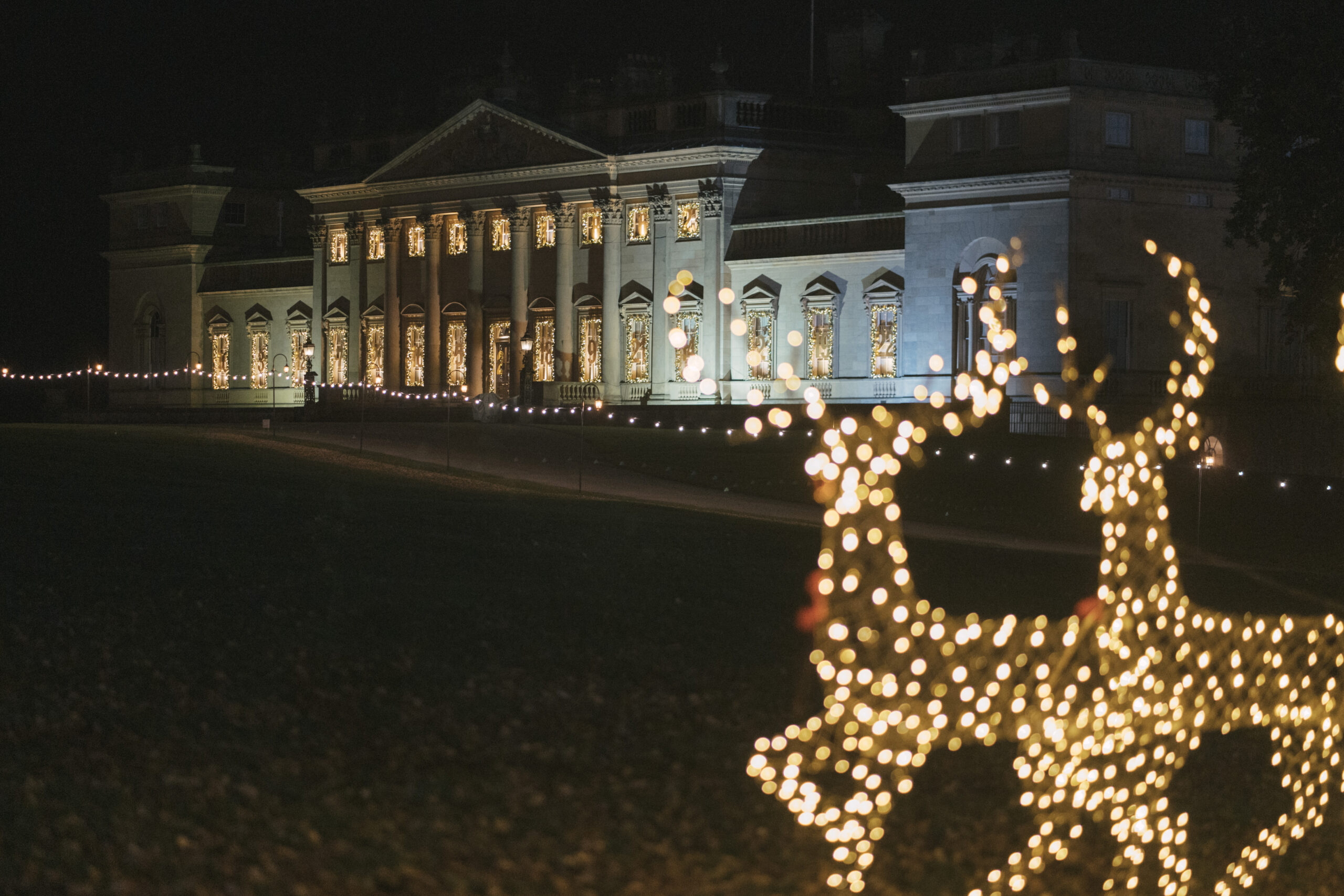 a large historic home facade in the dark with lit up deer garden ornaments in front