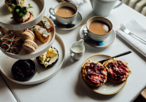 an afternoon tea laid out with cups of tea, a scone with jam and cream and a three tiered display of cakes