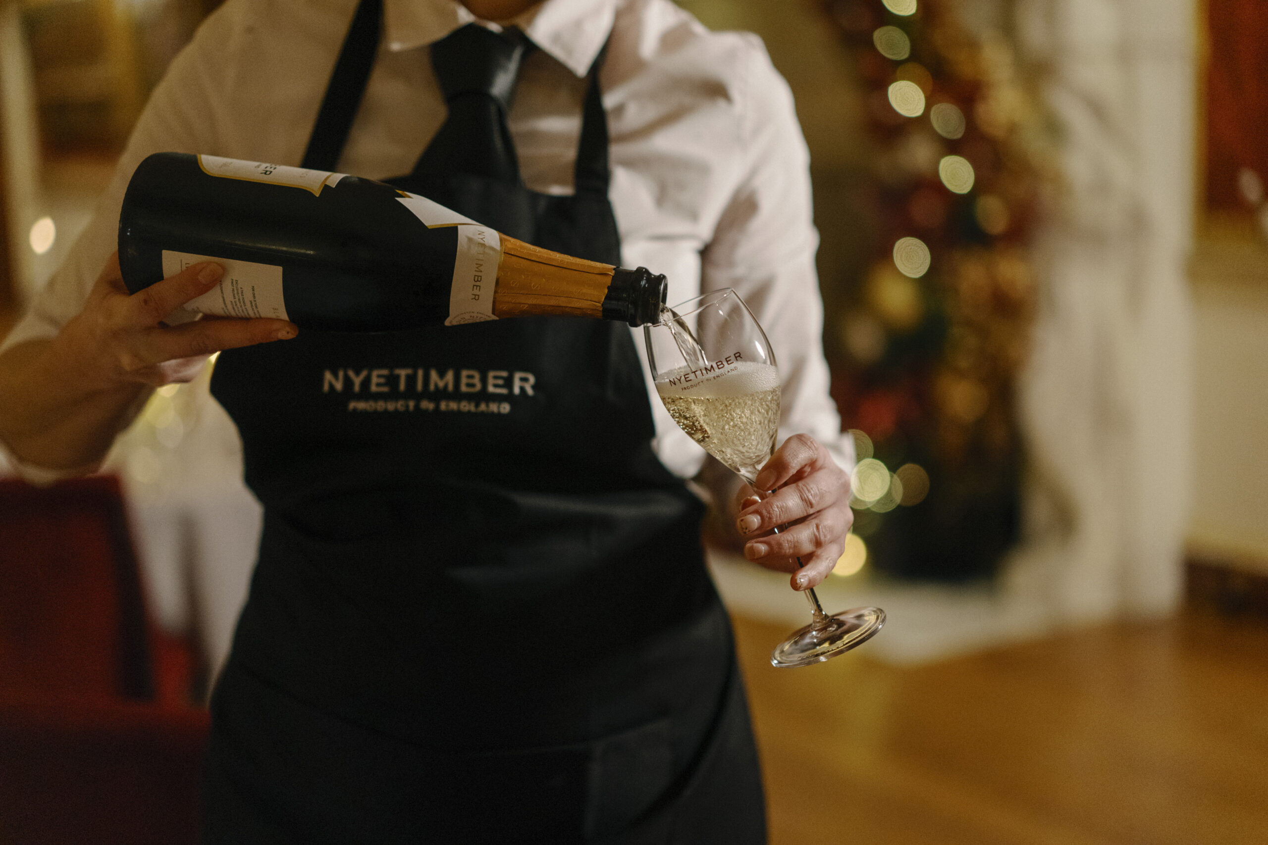 a server in a nyetimber branded apron pouring a glass of champagne